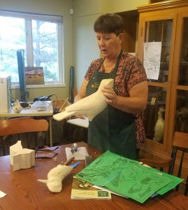 Michelle holding a block of wood that is being transformed into a crow. The kingfisher is laying on the table.